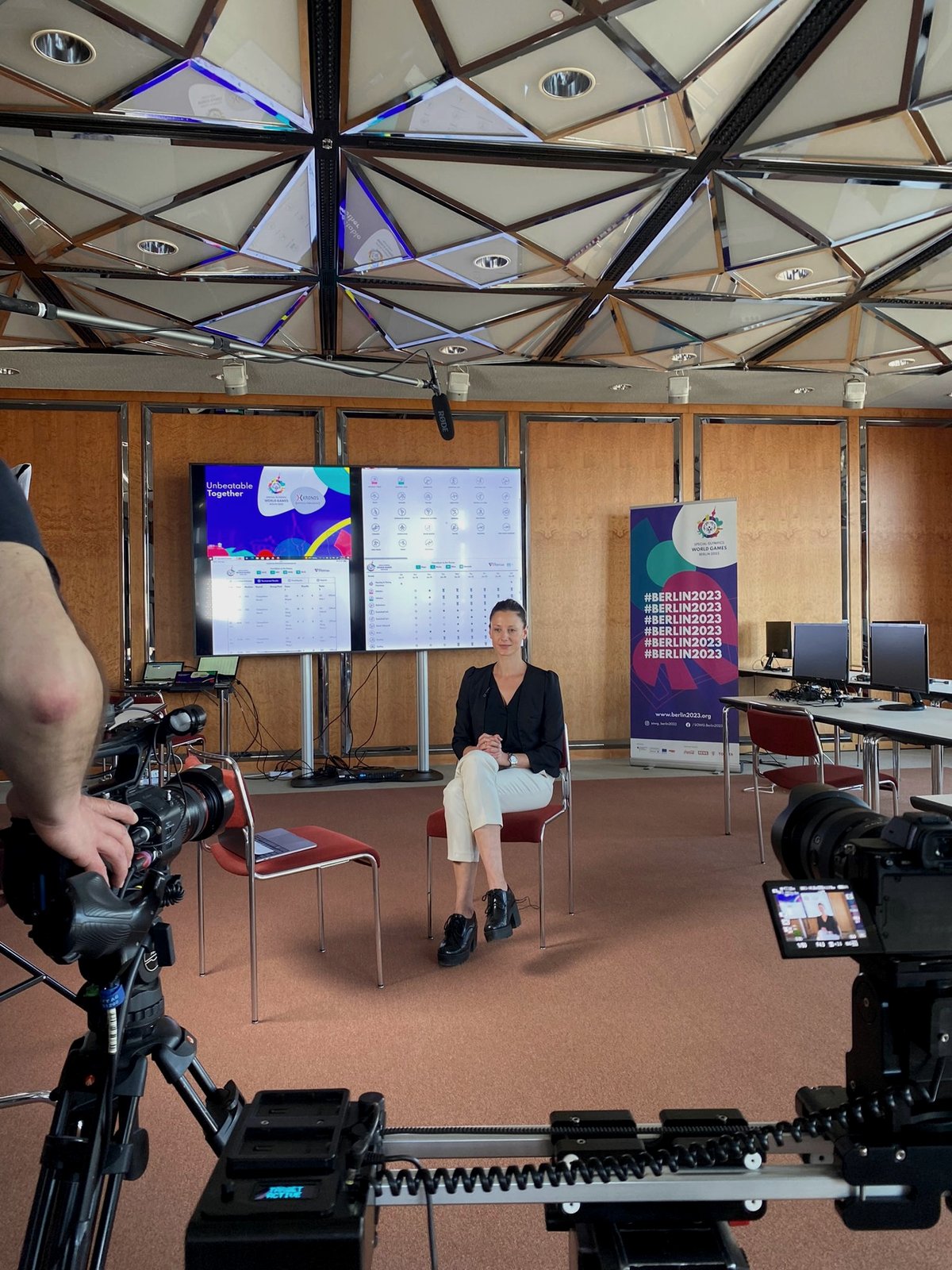 Bindi being filmed for an interview at Berlin 2023, results screens and cameras around her